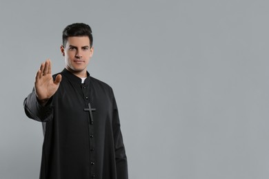 Photo of Priest wearing cassock with clerical collar on grey background, focus on hand. Space for text