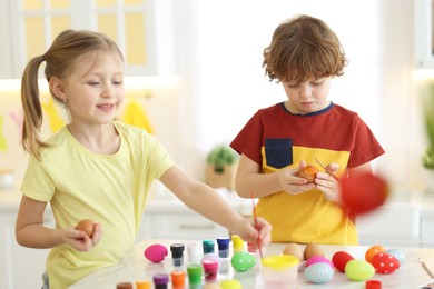 Photo of Easter celebration. Cute children painting eggs at white table in kitchen