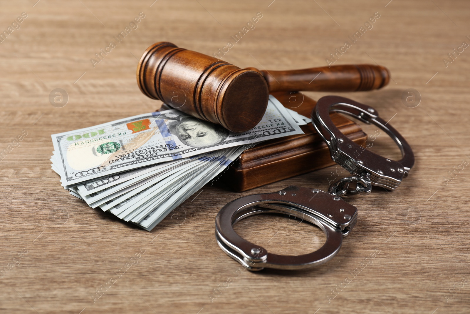 Photo of Judge's gavel, money and handcuffs on wooden table