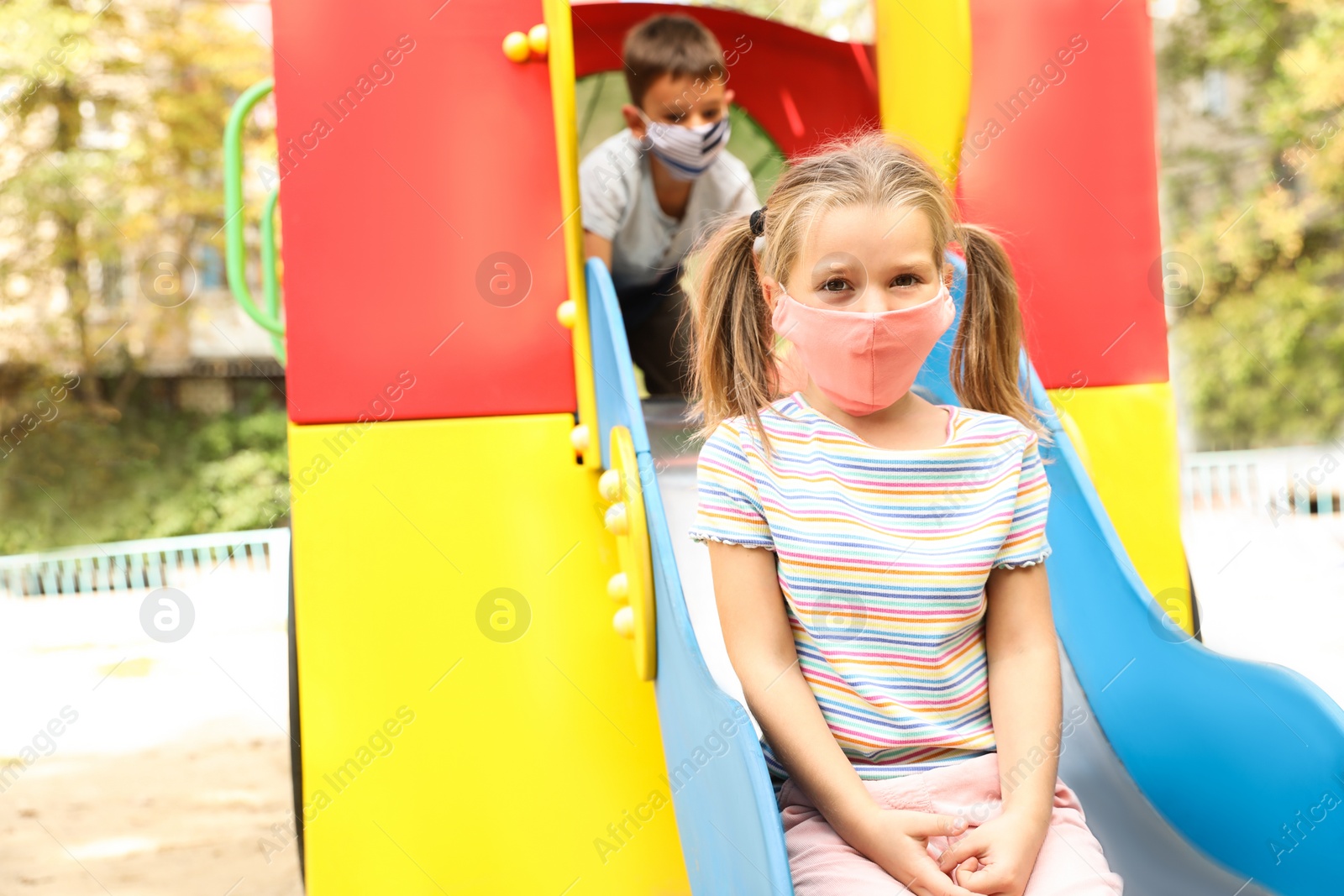 Photo of Little children with medical face masks on playground during covid-19 quarantine