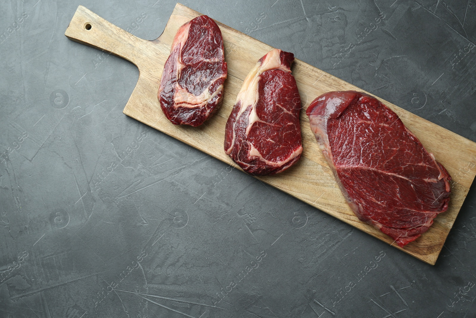 Photo of Wooden board with pieces of raw beef meat on grey table, top view. Space for text