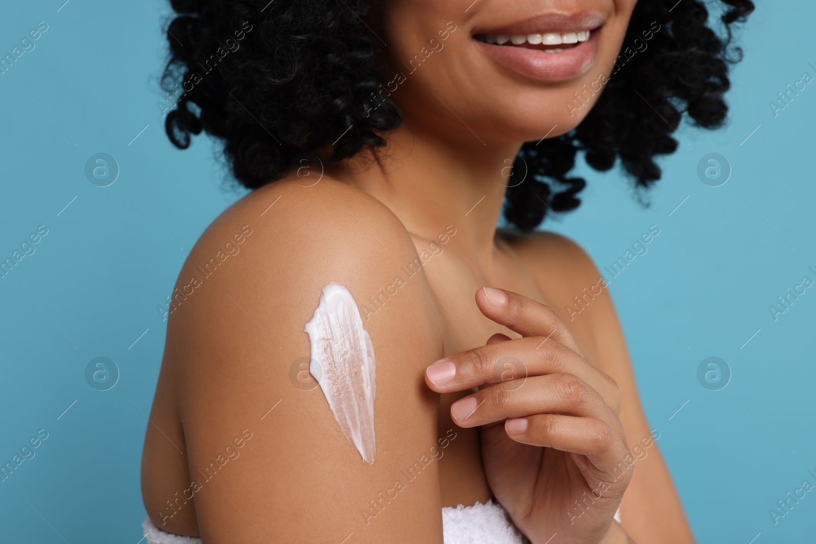 Photo of Young woman applying body cream onto shoulder on light blue background, closeup