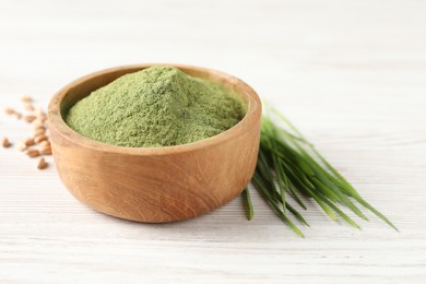 Wheat grass powder in bowl and fresh sprouts on white wooden table, closeup