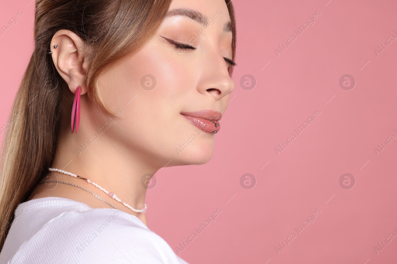 Photo of Young woman with lip and ear piercings on pink background, closeup. Space for text