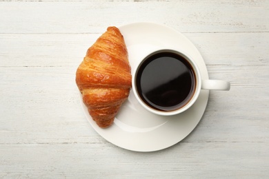Photo of Plate with cup of coffee and croissant on white wooden background, flat lay