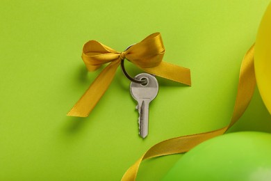 Key with yellow bow, ribbon and color balloons on light green background, flat lay. Housewarming party