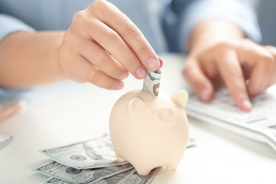 Woman putting money into piggy bank at table, closeup