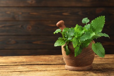 Photo of Mortar with pestle and fresh green lemon balm leaves on wooden table, space for text