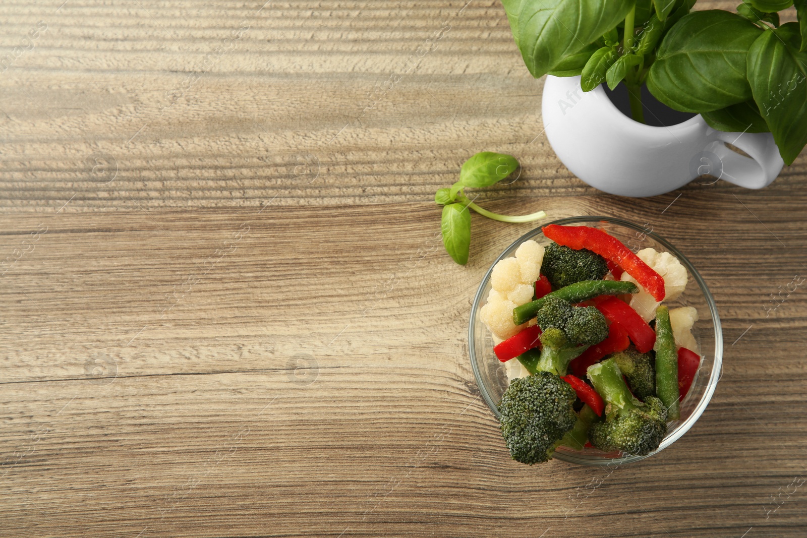 Photo of Frozen vegetables in bowl and basil on wooden table, flat lay. Space for text