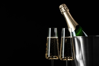 Glasses of champagne near bucket with bottle on black background, space for text