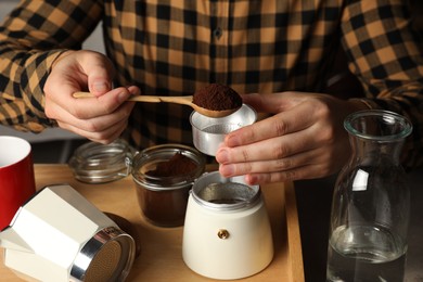 Photo of Man putting ground coffee into moka pot at table, closeup