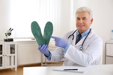 Photo of Senior male orthopedist showing insoles in clinic