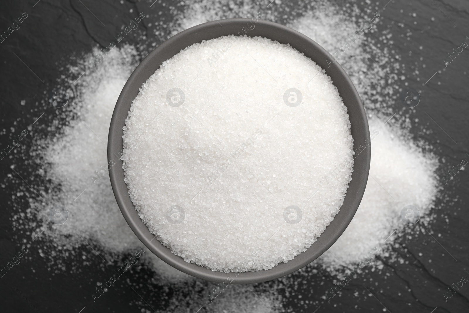 Photo of Granulated sugar on black table, top view