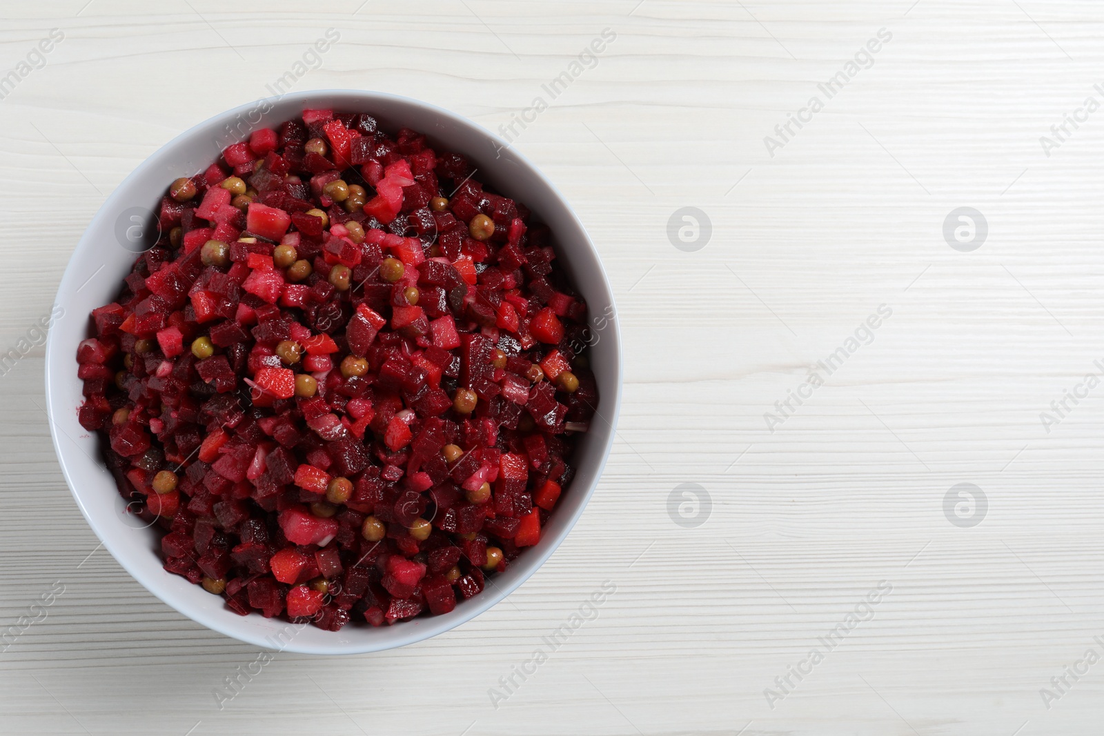 Photo of Bowl of delicious fresh vinaigrette salad on white wooden table, top view. Space for text