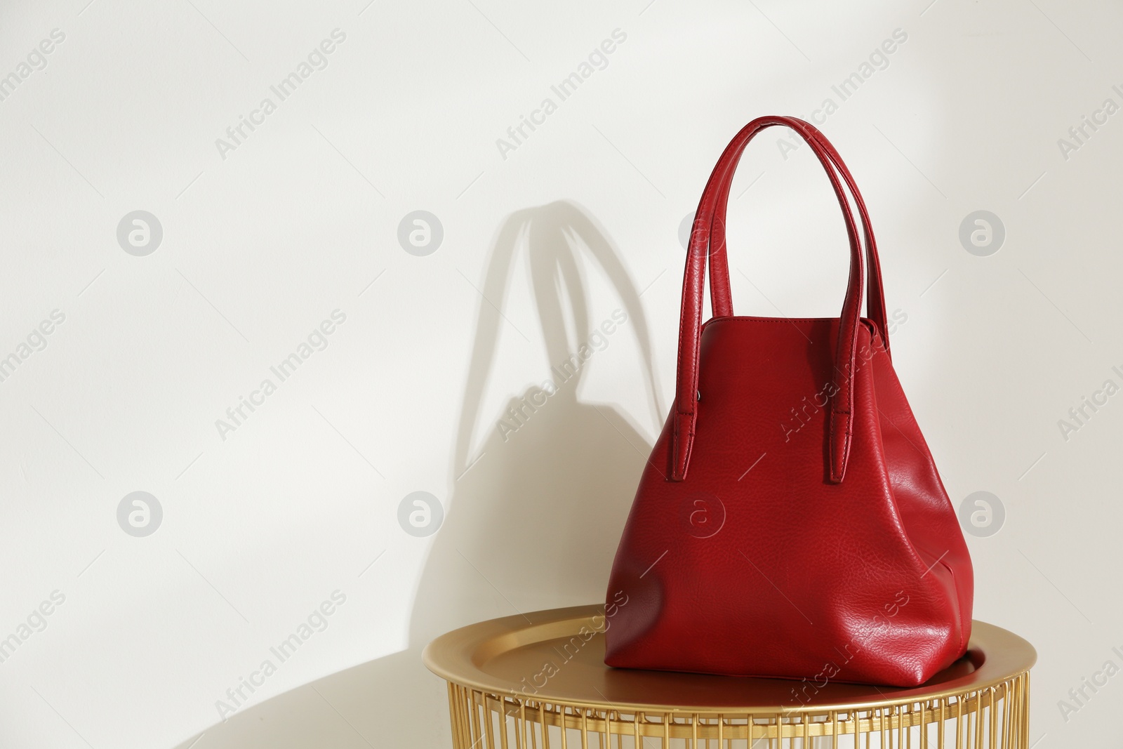 Photo of Stylish red woman's bag on table near light wall. Space for text