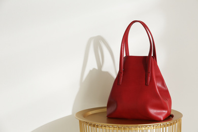 Stylish red woman's bag on table near light wall. Space for text