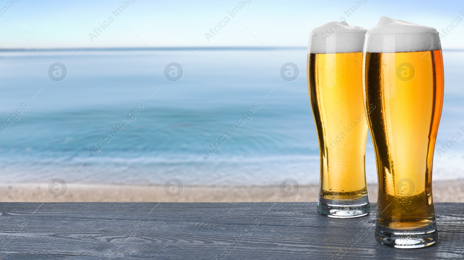 Image of Cold beer on wooden desk against blurred sea. Space for text