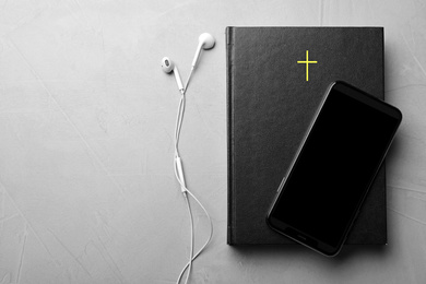 Bible, phone and earphones on light grey background, flat lay with space for text. Religious audiobook