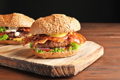 Photo of Tasty burgers with bacon on wooden board