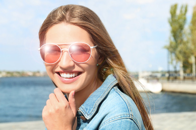 Image of Young woman wearing stylish sunglasses near river