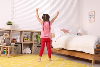 Photo of Cute little girl stretching in cosy bedroom, back view