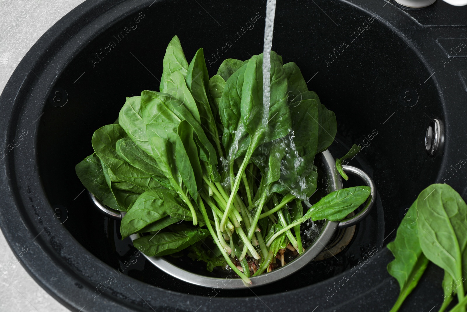 Photo of Washing fresh green healthy spinach in black sink, above view