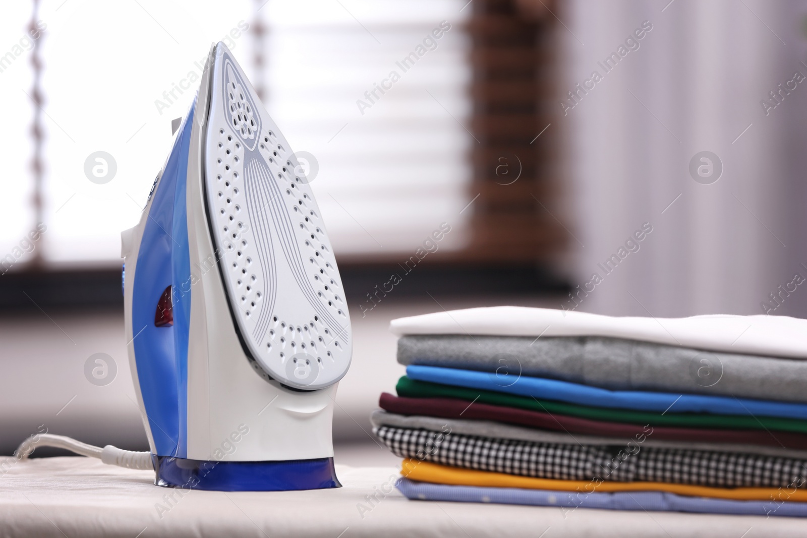 Photo of New modern iron and clean clothes on board indoors. Laundry day