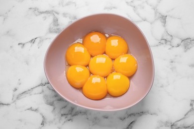 Photo of Bowl with raw egg yolks on white marble table, top view