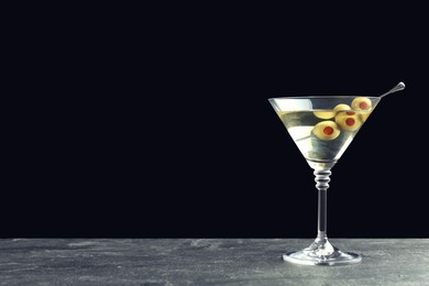 Photo of Martini cocktail with olives on grey table against dark background, space for text