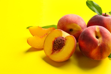 Photo of Fresh ripe peaches and green leaves on yellow background, closeup