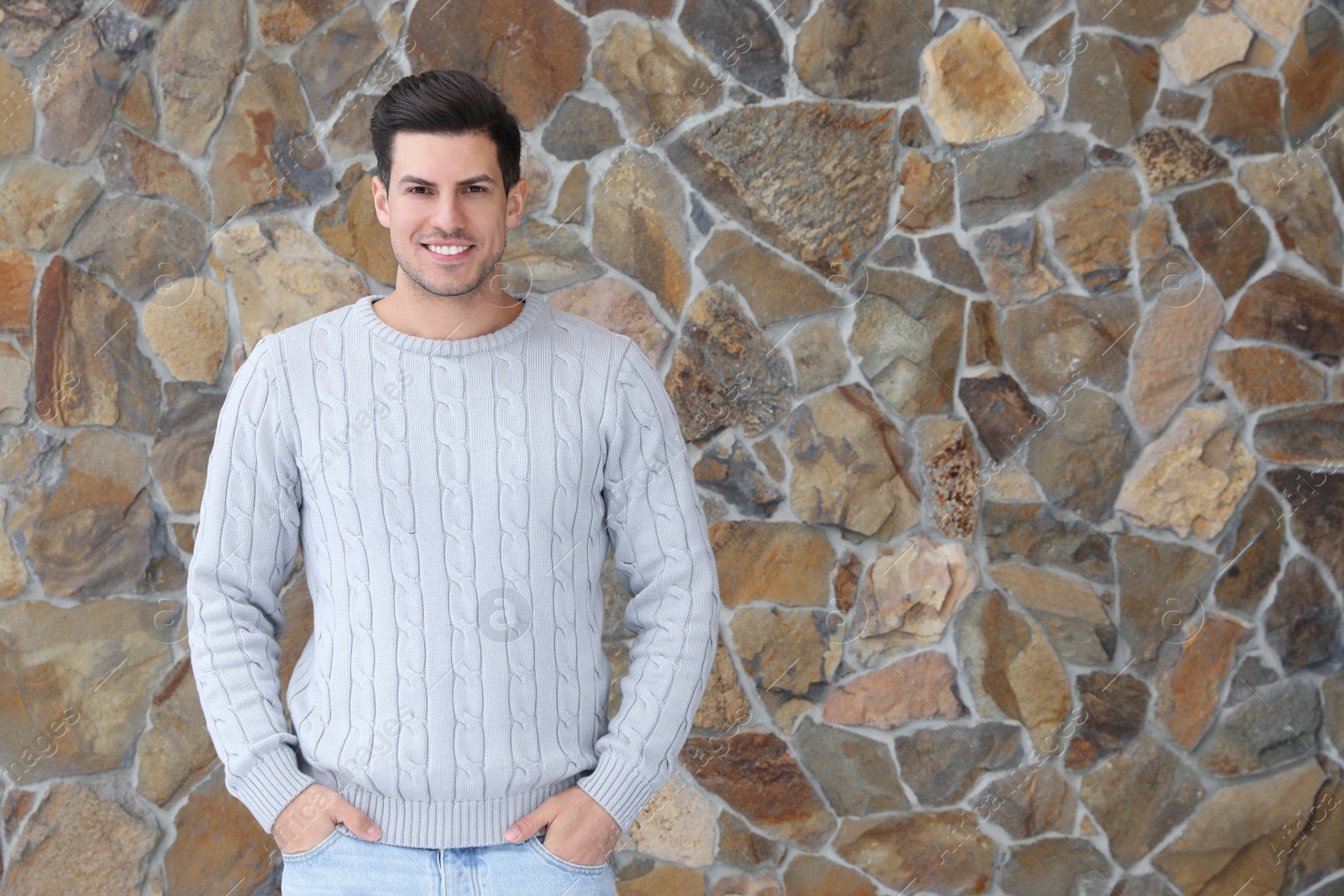 Photo of Happy man in warm sweater near stone wall. Space for text