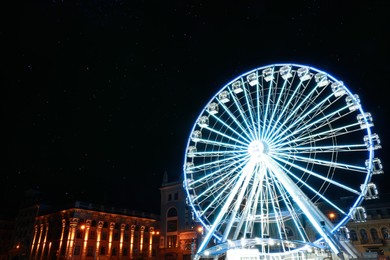 Photo of Beautiful glowing Ferris wheel on city street at night. Space for text