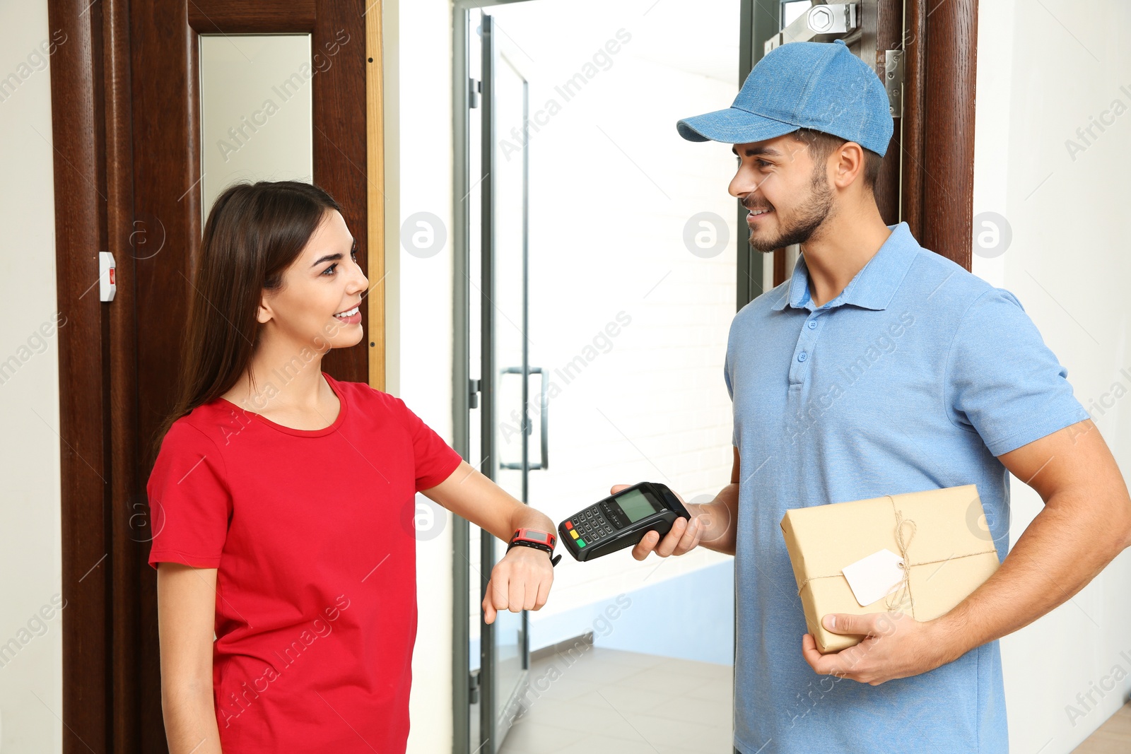 Photo of Woman with smartwatch using terminal for delivery payment indoors