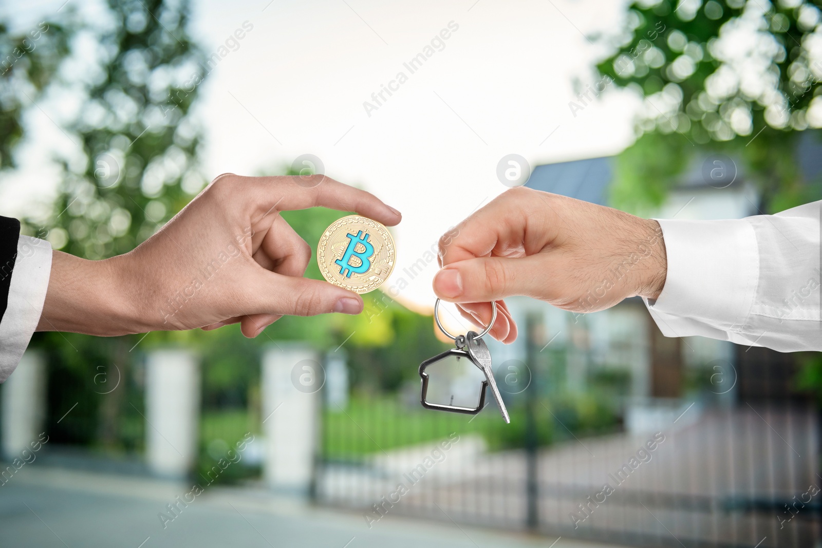 Image of Bitcoin exchange. Man using cryptocurrency to buy house. Seller holding key and buyer with bitcoin outdoors, closeup