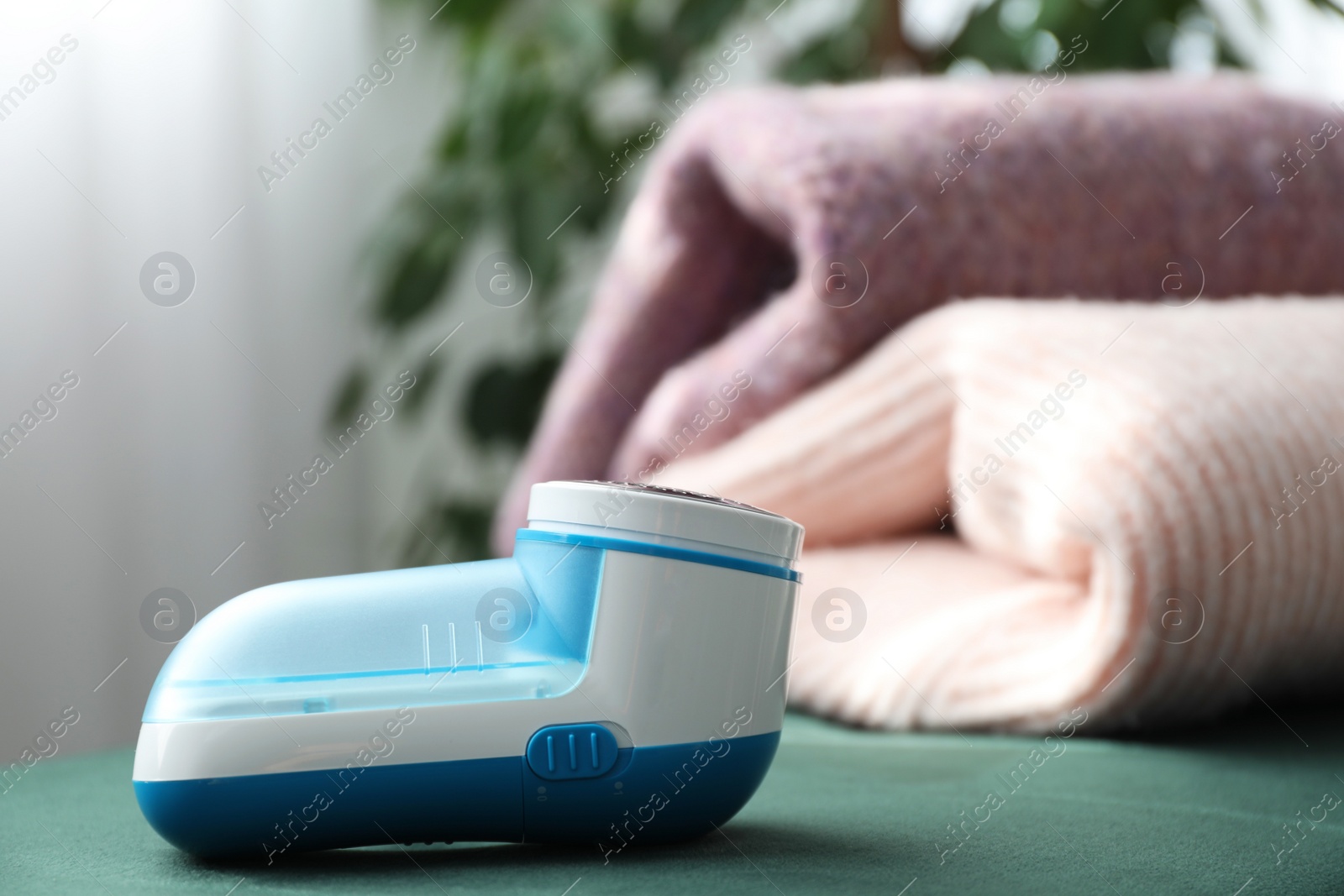 Photo of Modern fabric shaver and woolen sweaters indoors, closeup. Space for text