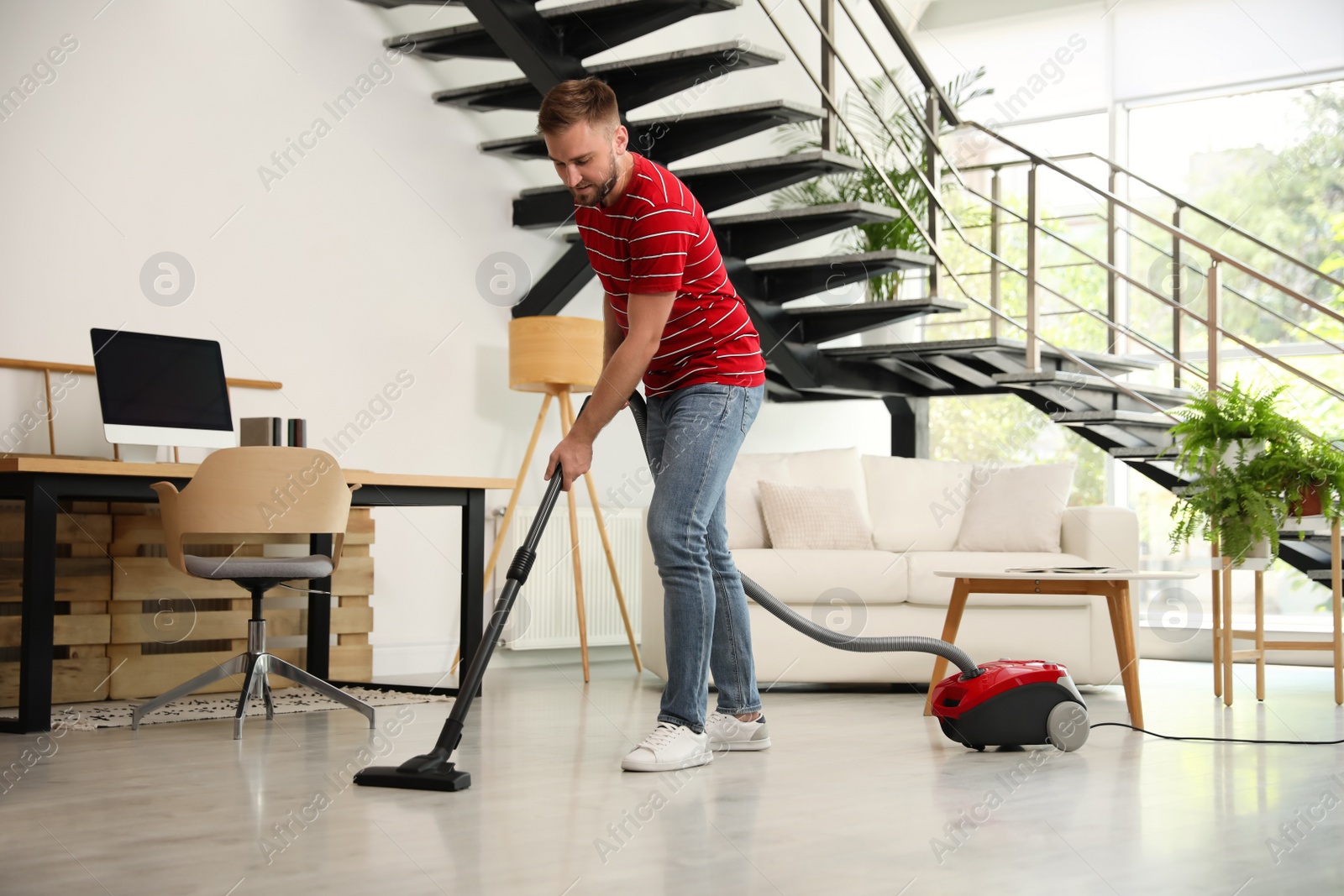 Photo of Young man using vacuum cleaner in living room