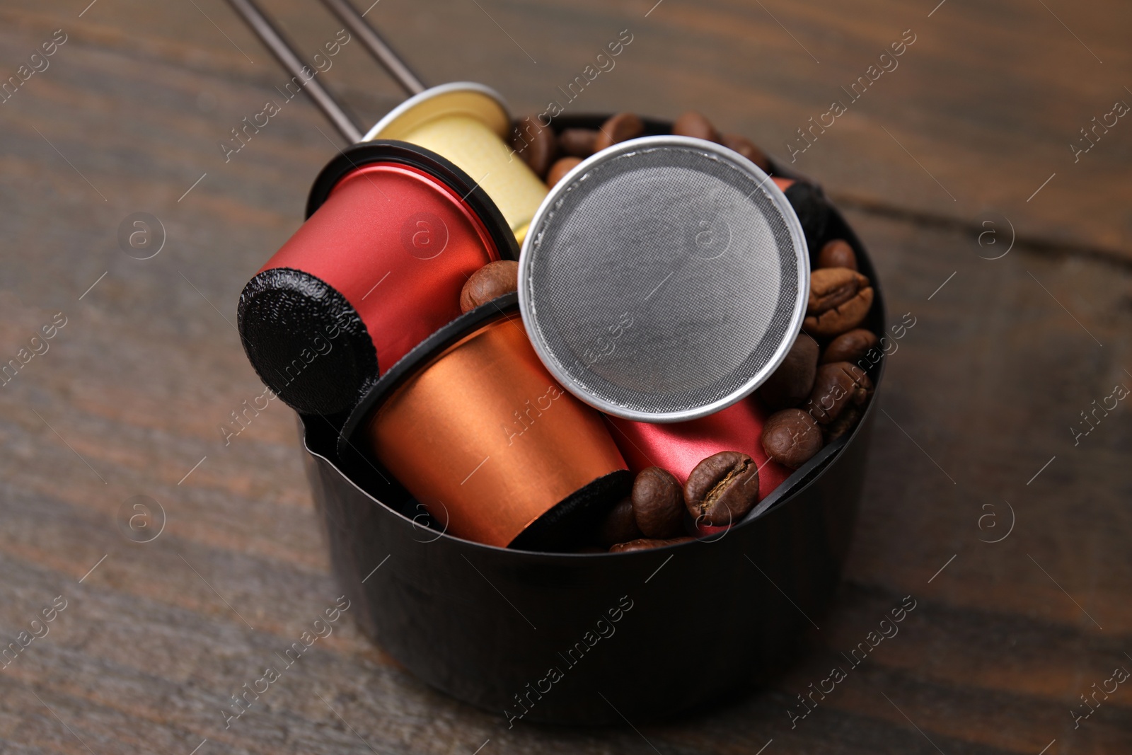 Photo of Saucepan with coffee capsules and beans on wooden table, closeup