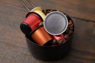 Photo of Saucepan with coffee capsules and beans on wooden table, closeup
