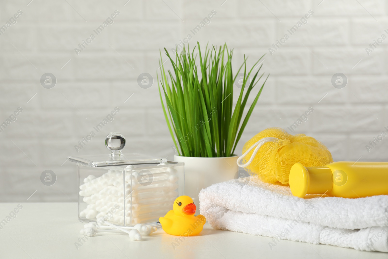 Photo of Baby cosmetic product, bath duck, cotton swabs and towel on white table against brick wall