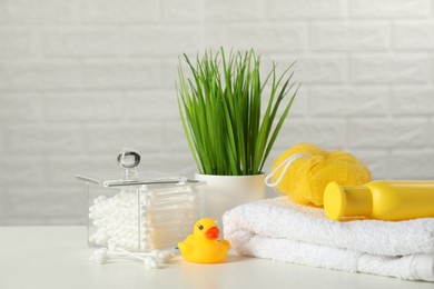 Baby cosmetic product, bath duck, cotton swabs and towel on white table against brick wall