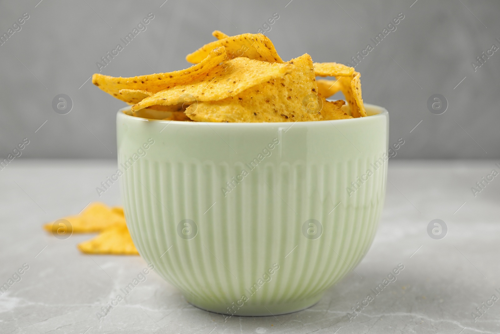 Photo of White bowl with tasty Mexican nachos chips on grey table