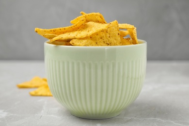 Photo of White bowl with tasty Mexican nachos chips on grey table