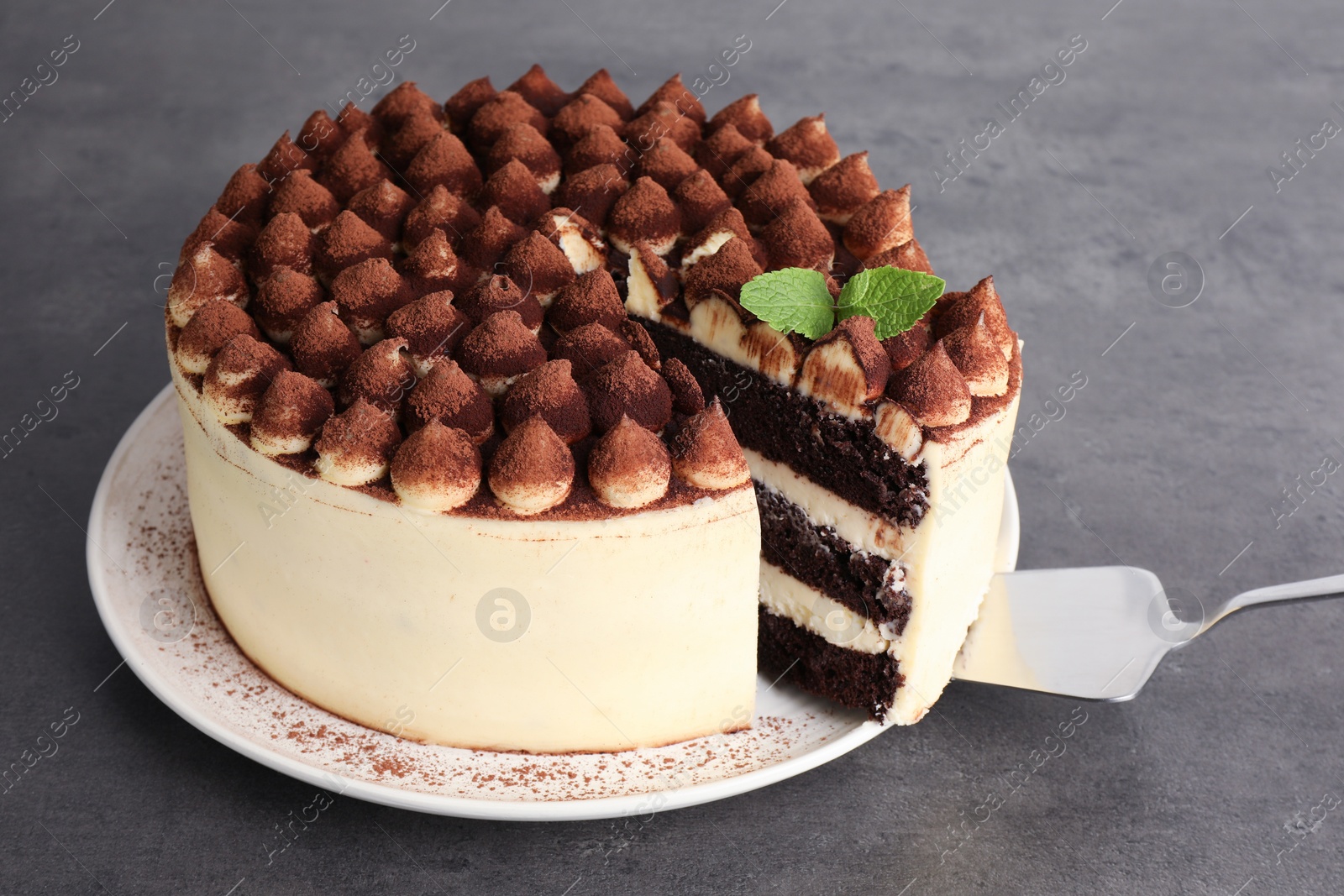 Photo of Delicious tiramisu cake with mint leaves and server on grey table