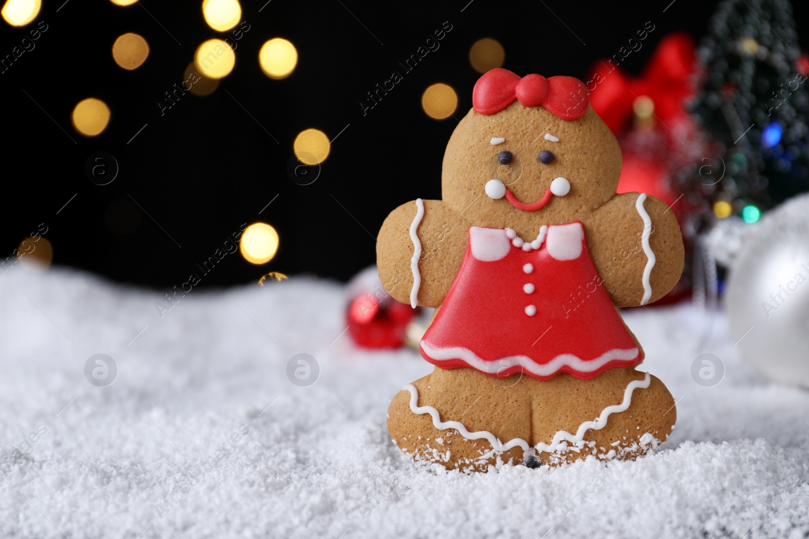 Photo of Gingerbread girl on snow against festive lights, closeup. Space for text