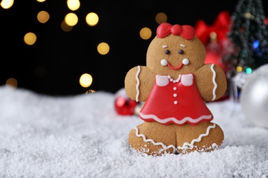 Photo of Gingerbread girl on snow against festive lights, closeup. Space for text