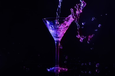 Photo of Pouring martini. Glass and splashes in neon lights on dark background