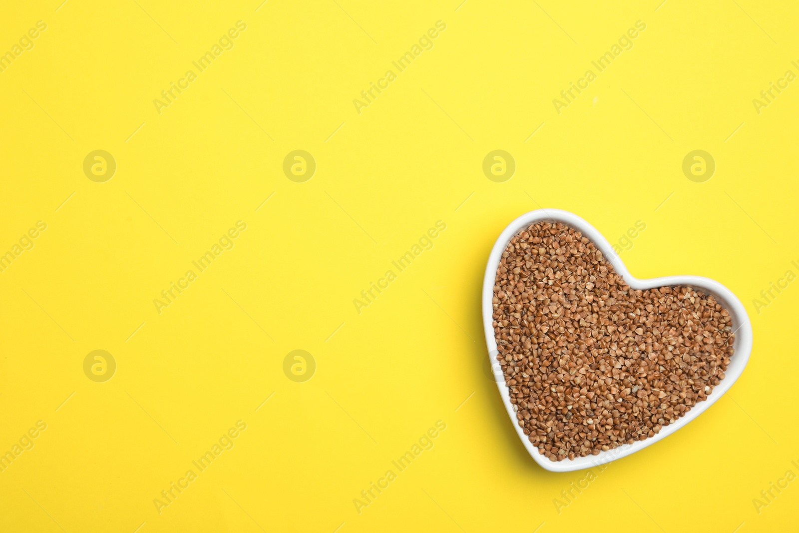 Photo of Buckwheat grains on yellow background, top view. Space for text