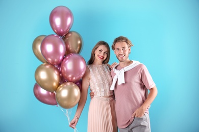 Young couple with air balloons on color background