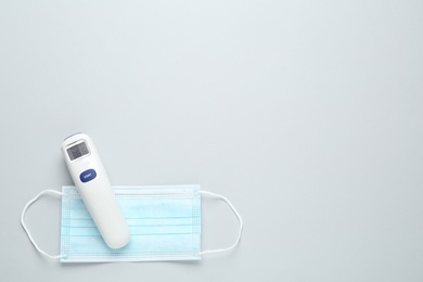 Photo of Infrared thermometer and medical mask on grey background, flat lay with space for text. Checking temperature during Covid-19 pandemic