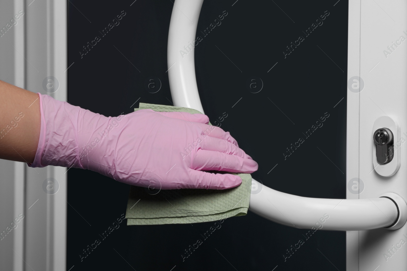 Photo of Woman in glove cleaning door handle with paper towel indoors, closeup